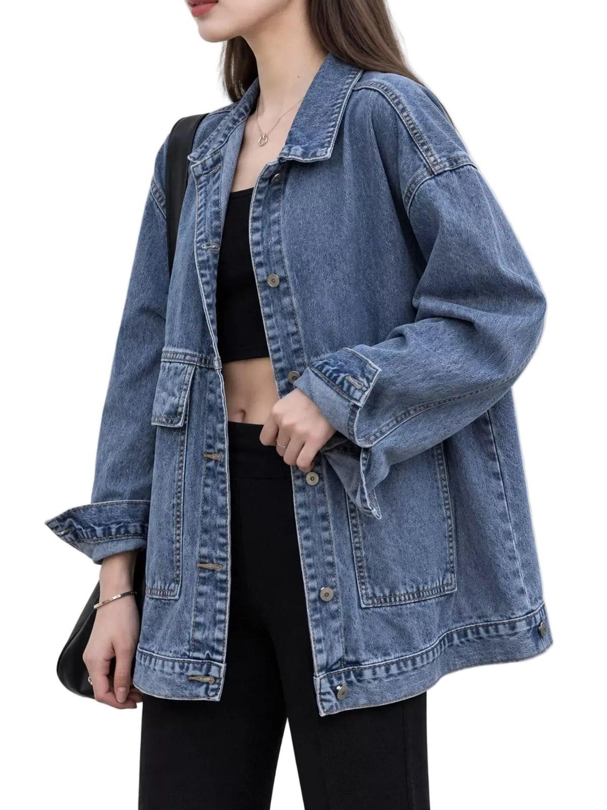 A woman wearing an oversized medium-wash blue denim jacket over a black crop top and black pants, photographed against a plain light background.