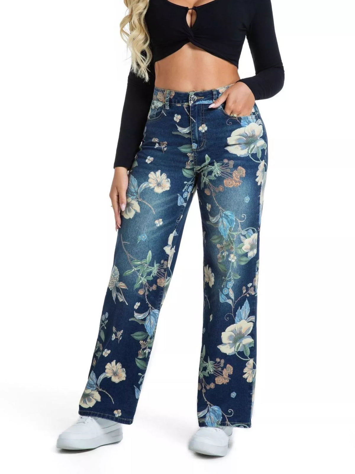 A model wearing high-waisted, wide-leg blue jeans with a floral print, paired with a black long-sleeve crop top and white sneakers, shown against a plain white background.