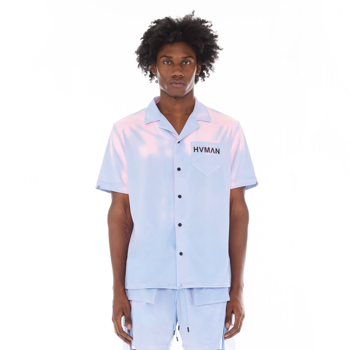 Person wearing a light blue shirt with pink sleeves and 'HVMAN' branding on a white background
