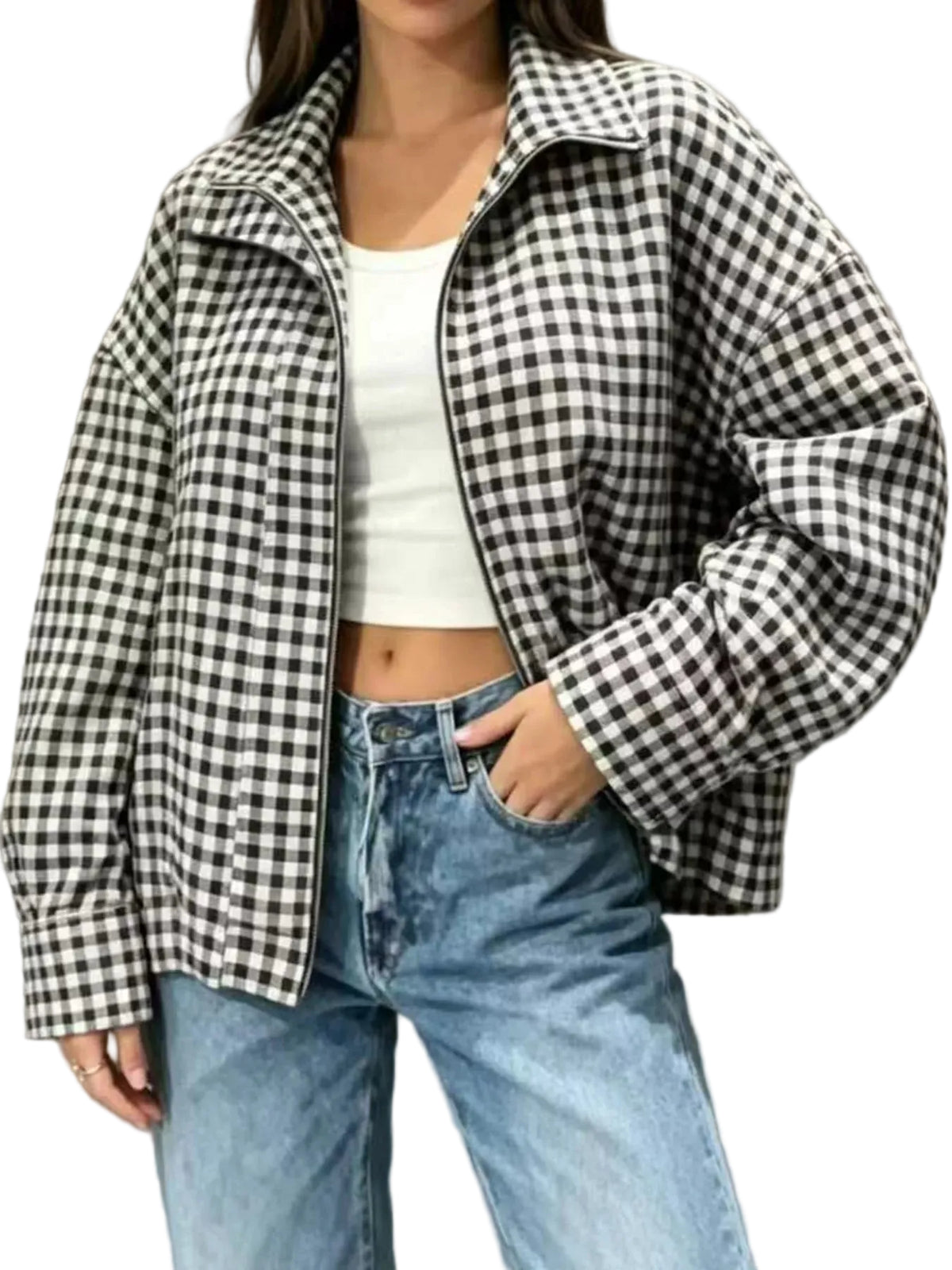 A woman wearing a black and white gingham zip-up jacket over a white crop top and light blue jeans, standing against a neutral gray wall.