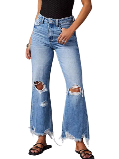 A person wearing light-wash blue distressed flare jeans with ripped knees and frayed hems, paired with a black sleeveless top and black strappy sandals, against a plain gray studio background.