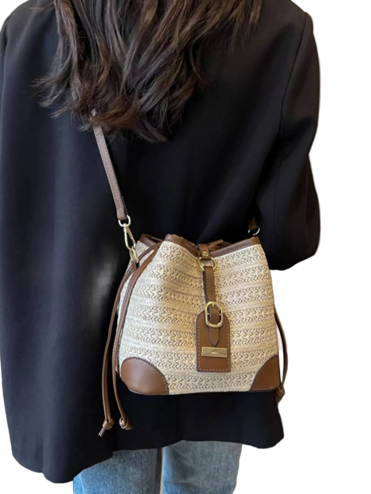 A person wearing a black blazer and light blue jeans carries a beige and brown woven bucket bag with a leather strap and gold-tone hardware.