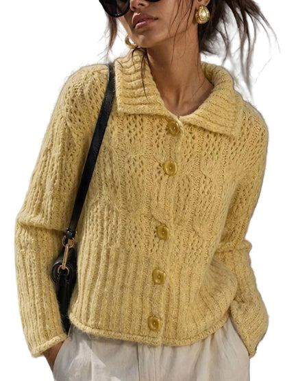 A woman wearing a fuzzy pale yellow cable-knit cardigan with matching buttons, styled with white pants and a black shoulder bag in an outdoor street setting.