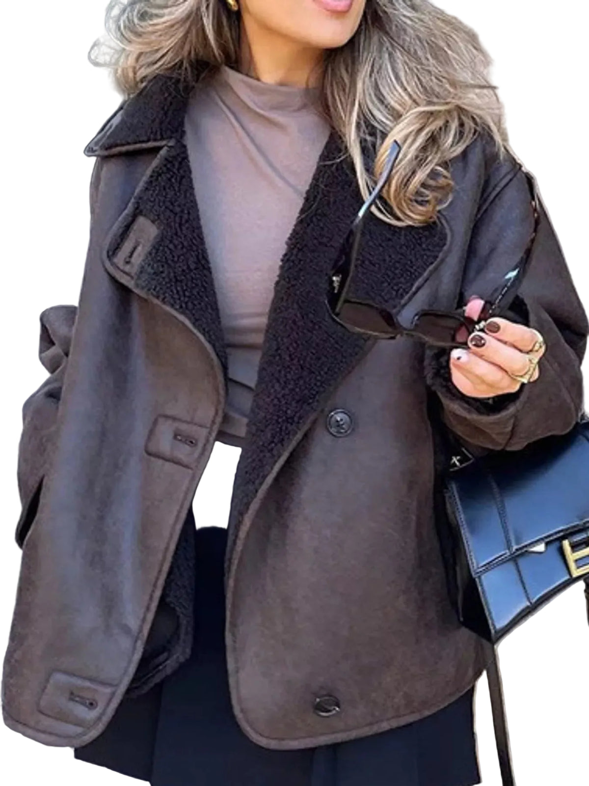 A woman wearing a brown suede-like jacket with a dark brown sherpa lining, styled over a taupe top and black skirt, holding sunglasses and a black handbag.