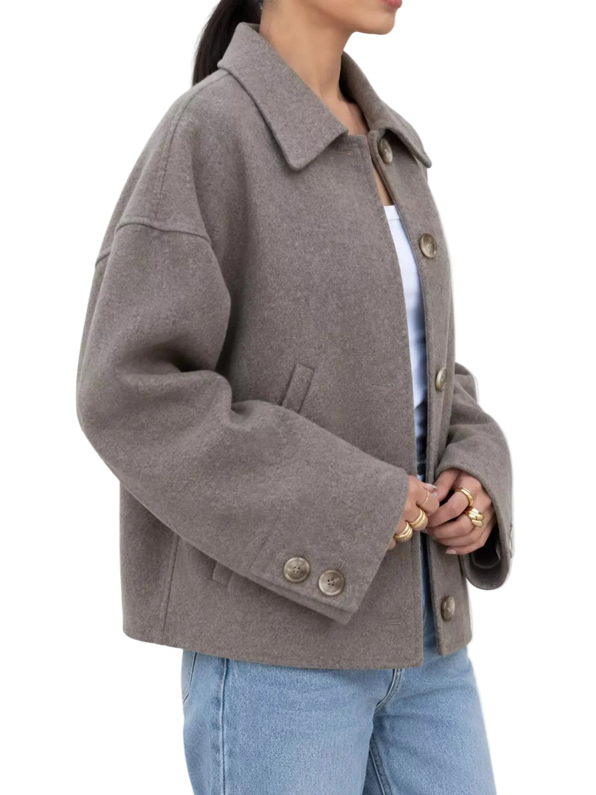 A woman wearing a taupe-brown oversized button-front coat with a collar, paired with a white top and light blue jeans, shown from the side against a plain white background.
