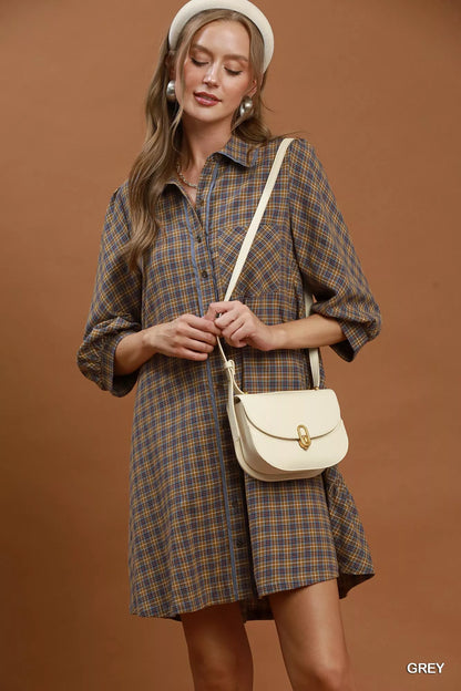 Woman wearing a plaid dress holding a beige handbag against a brown background