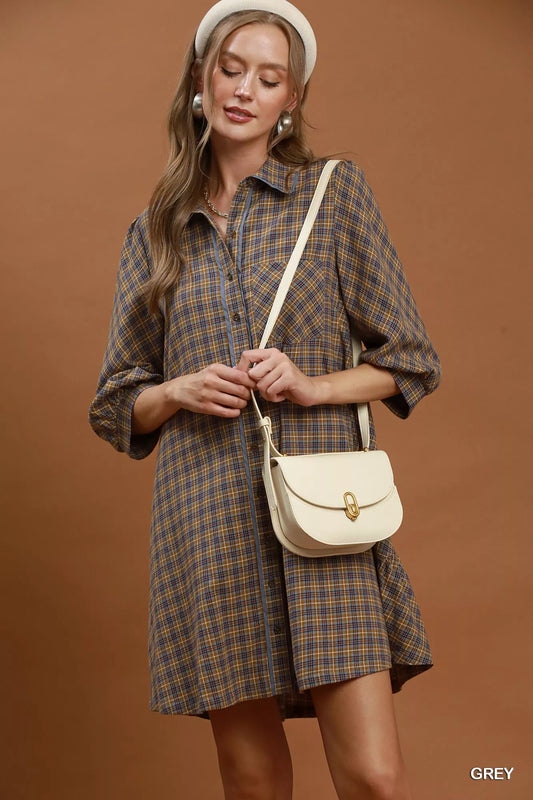 Woman wearing a plaid dress holding a beige handbag against a brown background