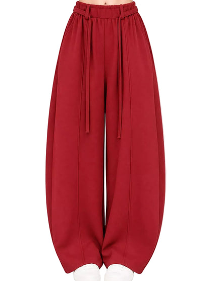 A pair of wide-leg, balloon-style pants in a deep red or burgundy color, featuring an elastic waistband with hanging drawstrings, shown on a model from the waist down against a plain white background.