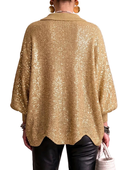 A person shown from the back wearing a shimmering gold knit poncho-style cardigan with wide draped sleeves and a scalloped hem, paired with black pants against a neutral textured wall.