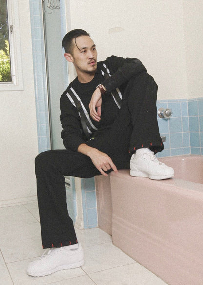 Person wearing a black outfit with white accents sitting on a pink bathtub in a bathroom.