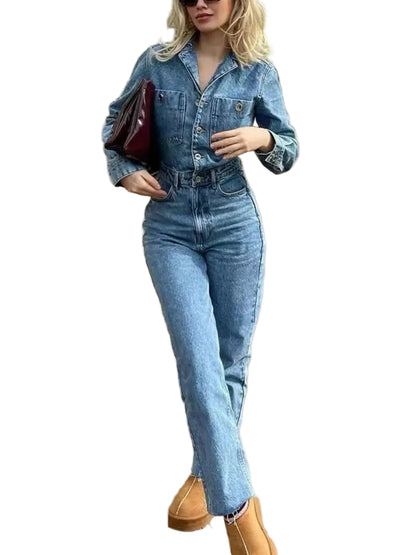 A woman wearing a light-wash blue denim jumpsuit with a button-up shirt collar and long sleeves, paired with tan boots and carrying a dark red bag, standing on a wooden deck.