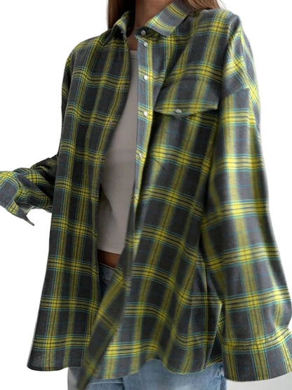 A woman wearing an oversized long-sleeve plaid button-up shirt in dark gray, yellow, and green, layered over a white top and blue jeans.