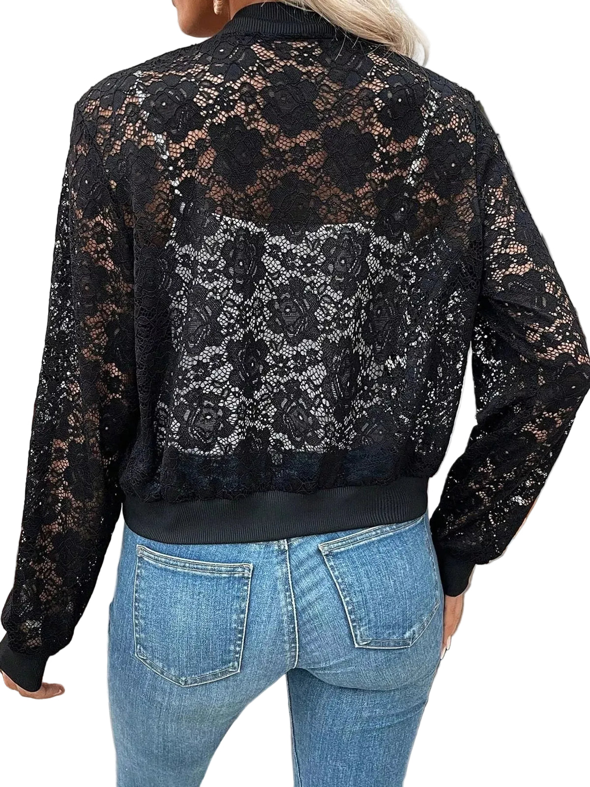 A woman viewed from the back wearing a black lace bomber jacket with floral lace panels and ribbed collar, cuffs, and hem, paired with blue jeans in an outdoor patio setting.
