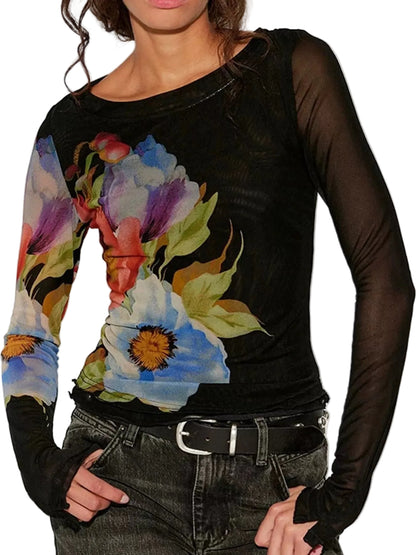A woman wearing a sheer black long-sleeve top with a vibrant multicolor floral print on the front, paired with dark gray jeans and a black belt.