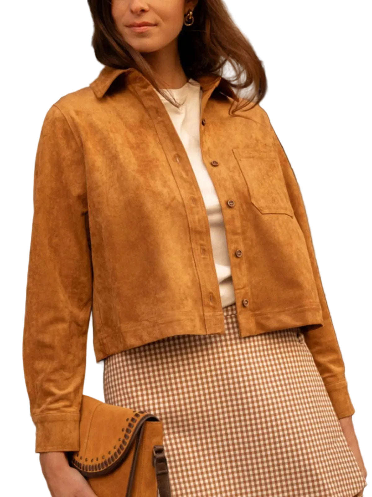 A woman wearing a cropped tan suede button-up shirt jacket over a white top and a beige-and-white gingham skirt, holding a matching tan suede clutch bag.