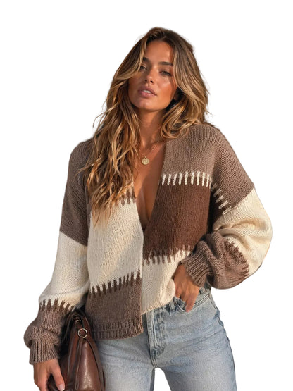 A woman wearing a cozy knit cardigan with brown, cream, and beige geometric patterns, paired with light blue jeans, standing in front of a rustic wooden door.