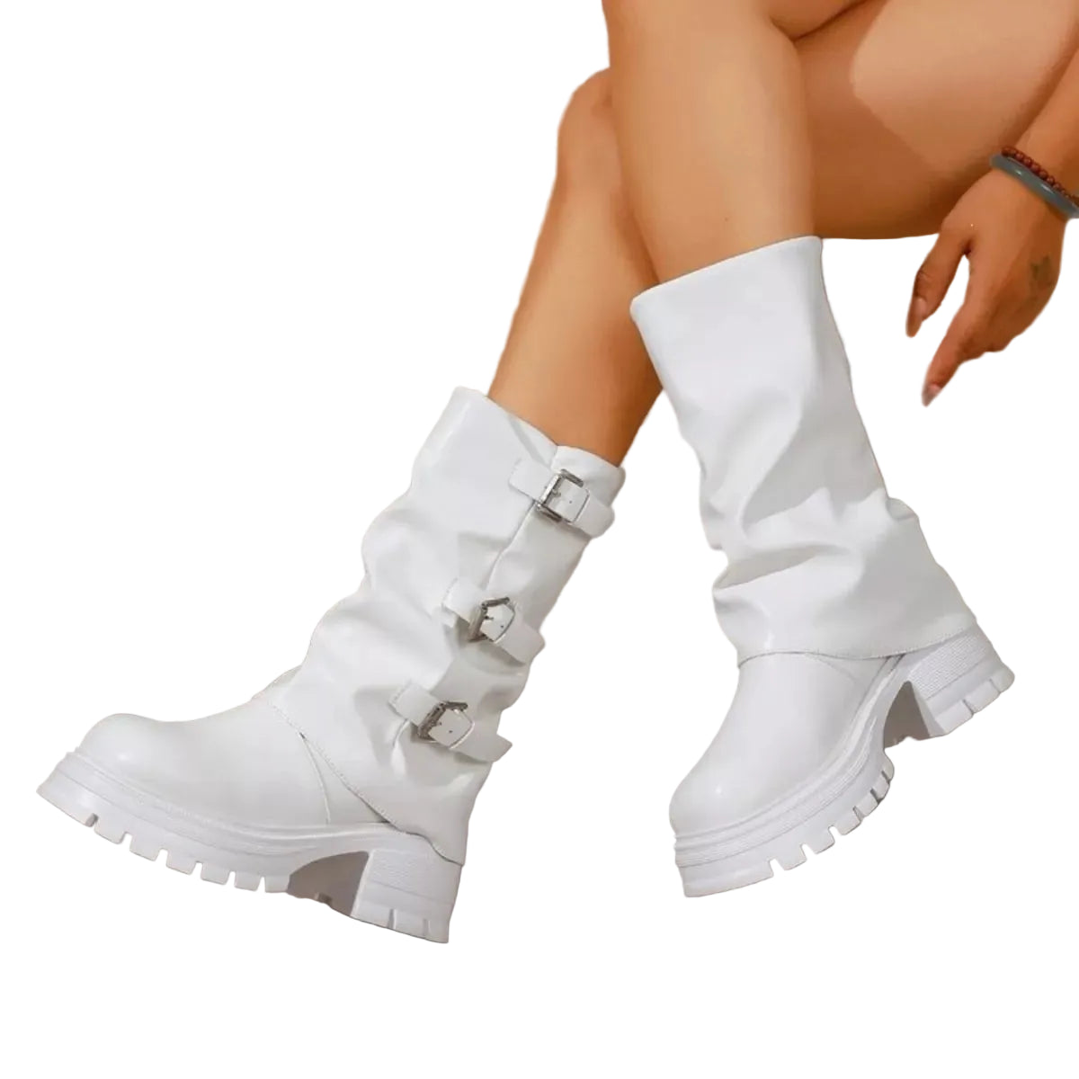 White slouchy mid-calf boots with buckle straps and chunky lug soles, shown on a model's feet against a stone-tile wall background.