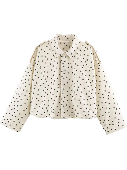An off-white long-sleeve blouse with a black polka dot pattern, featuring a pointed collar and shoulder epaulets, shown against a plain white background.