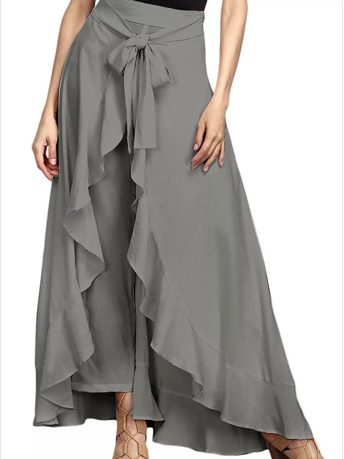 A woman wearing a high-waisted, flowing gray wrap skirt with layered ruffles and a side tie, paired with brown strappy heels against a plain white background.