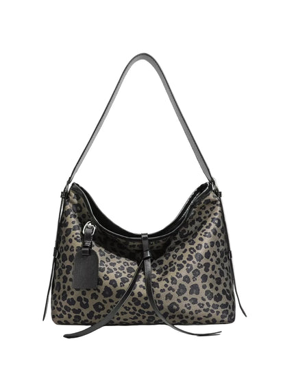 A leopard print shoulder bag with black leather trim, a single shoulder strap, and a hanging black leather tag, shown against a light gray background.