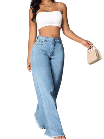 A woman wearing a white spaghetti-strap crop top and light-wash wide-leg denim jeans with frayed hems, holding a small beige handbag against a gray concrete wall.