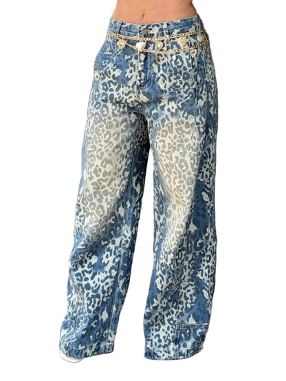 Wide-leg blue and white leopard-print jeans with a decorative gold chain belt detail at the waist, shown on a model standing against a dark brown paneled wall.