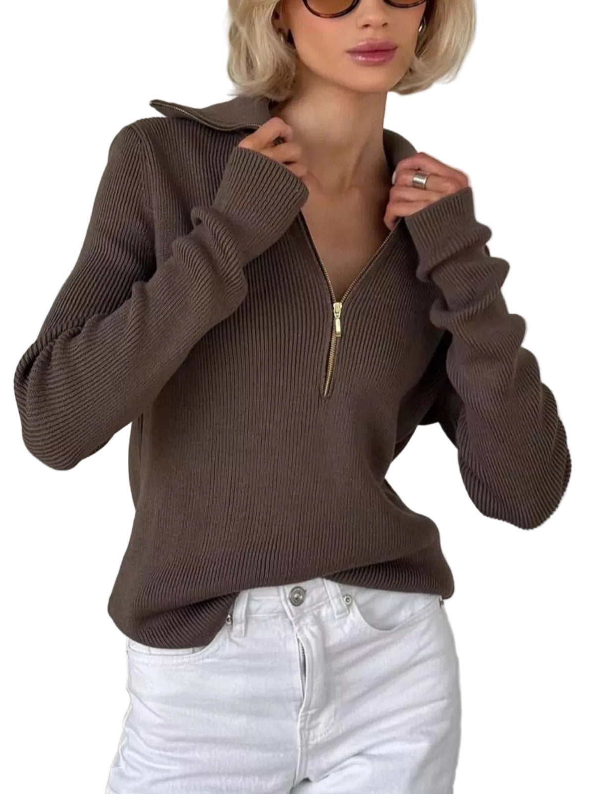 A woman wearing a ribbed brown half-zip sweater with a stand collar and white jeans, standing indoors against a white paneled wall.