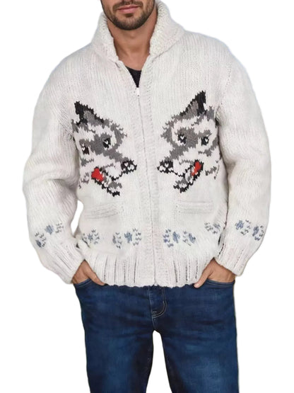 A man wearing a cream-colored knit zip-up sweater with a detailed gray and black raccoon design on the front, paired with blue jeans, set against a blurred outdoor background of a grassy field and blue sky.