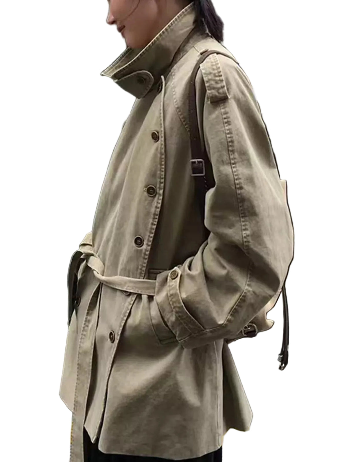A person wearing a light khaki trench coat with a belted waist, shown in profile outdoors next to a black car.