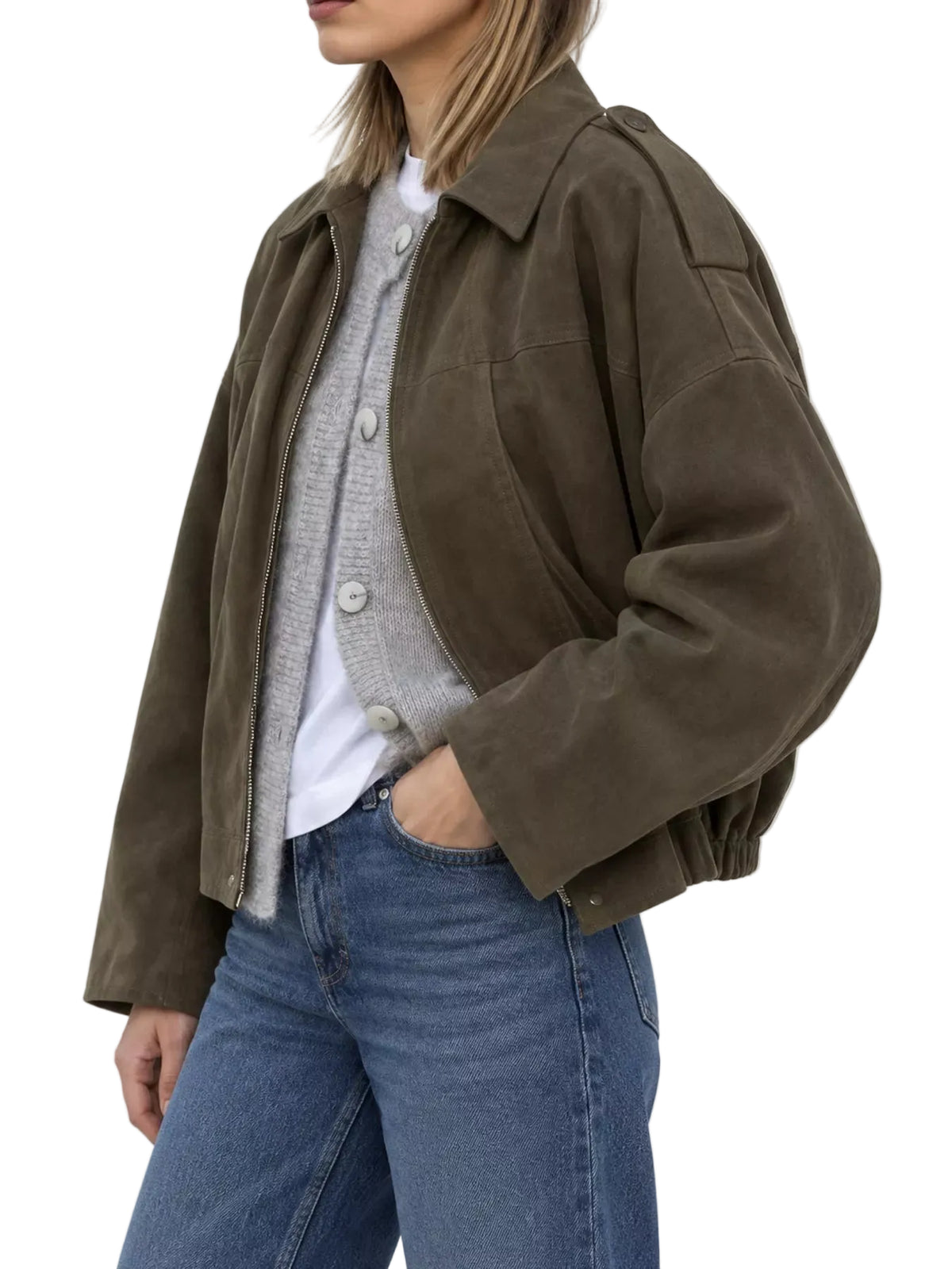 A woman wearing an oversized dark olive brown suede jacket over a gray cardigan and white t-shirt, paired with blue jeans, photographed against a light gray studio background.