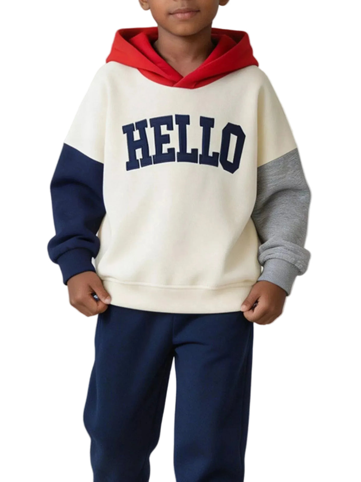 A child wearing a color-blocked hoodie with a cream body, red hood, navy sleeves, and gray cuffs, featuring the word 'HELLO' in navy across the chest. The child is also wearing navy sweatpants, standing indoors next to a basket with sports balls.