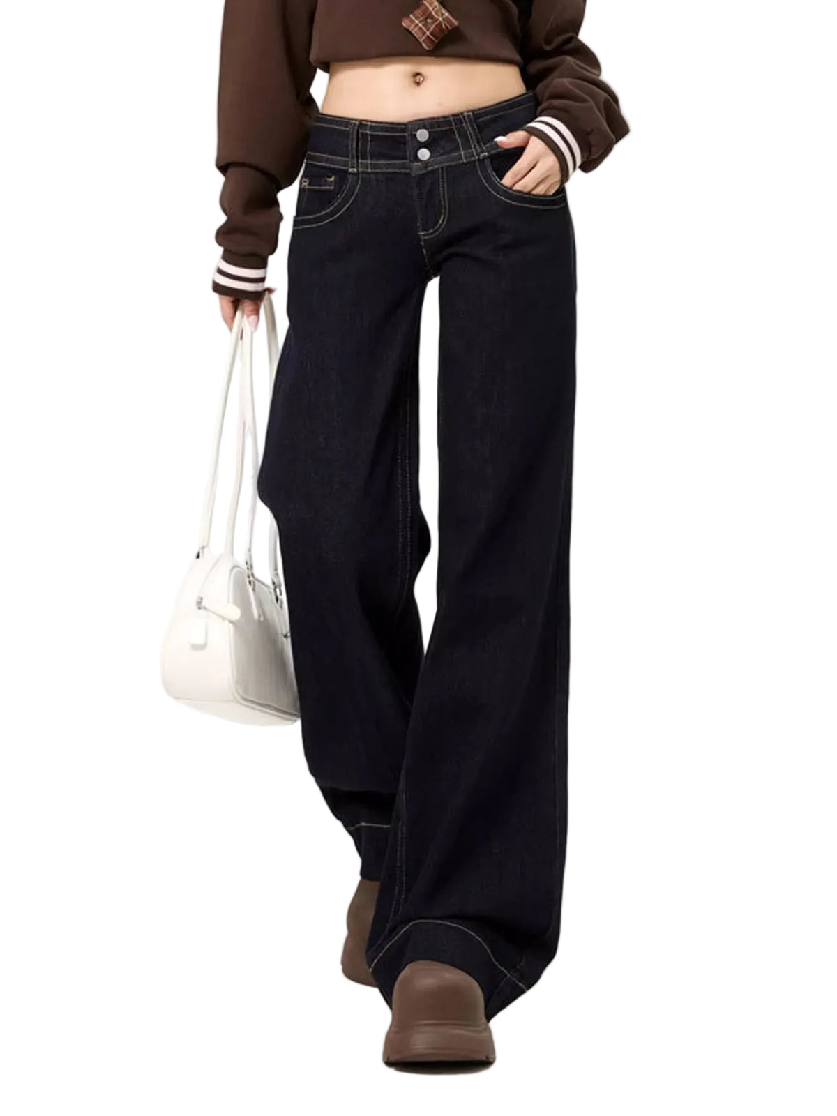 A model wearing dark wash wide-leg jeans, a brown cropped sweatshirt with striped cuffs, and brown slip-on shoes, holding a white handbag against a plain white background.