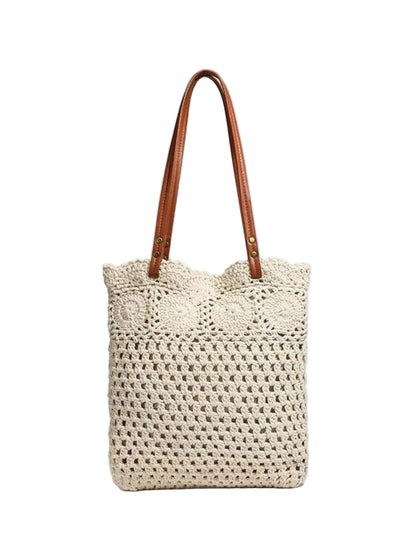 A cream-colored crocheted tote bag with brown leather shoulder straps, shown against a light gray background.