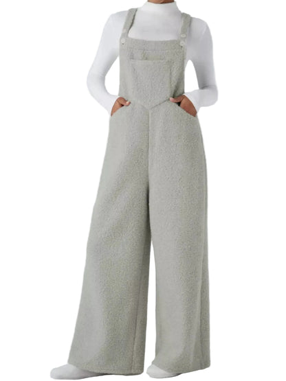 A model wearing light gray wide-leg overalls with a textured bouclé-like fabric, styled over a white long-sleeve top against a light gray studio background.