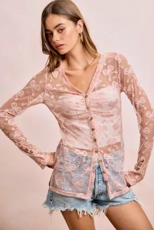 Woman wearing a pink lace cardigan over a denim outfit on a light pink background