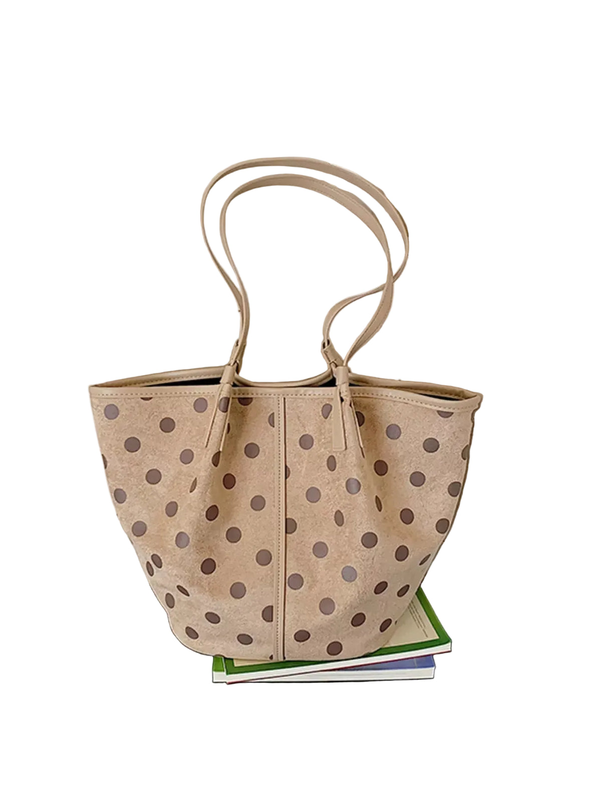 A beige canvas tote bag with brown polka dots, featuring dual shoulder straps, resting on a stack of books on a black bench against a white paneled wall.