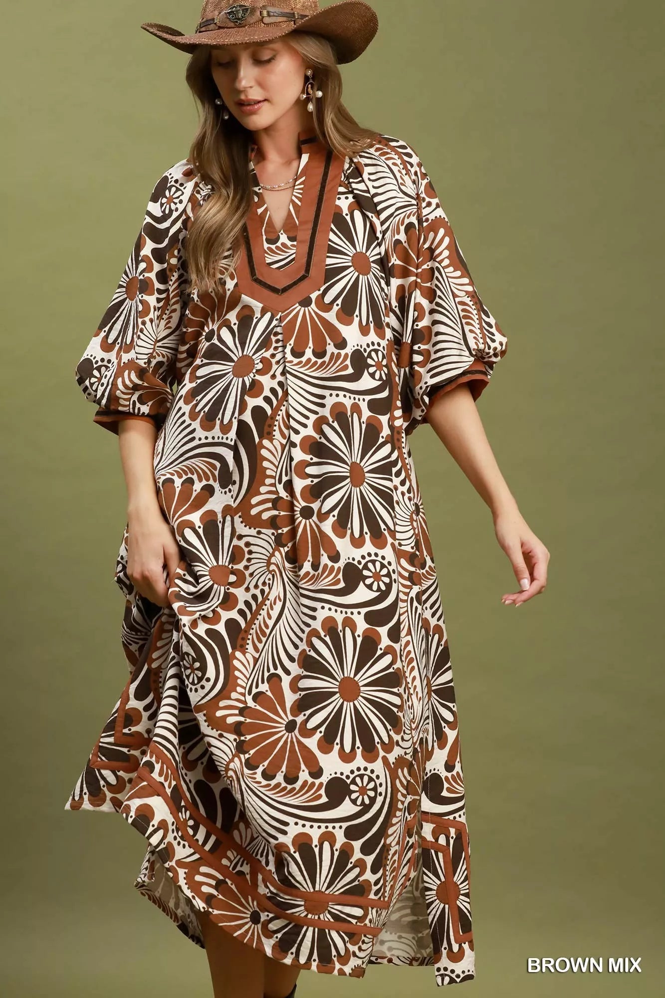 Woman wearing a patterned dress with a brown hat against a green background