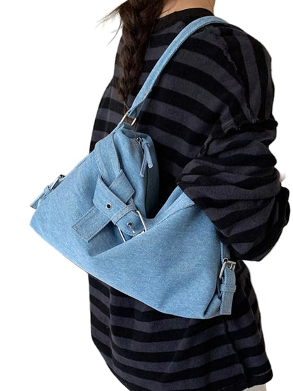 A person wearing a black and navy striped shirt carries a light blue denim shoulder bag with a wide strap and front flap pocket in an indoor room setting.