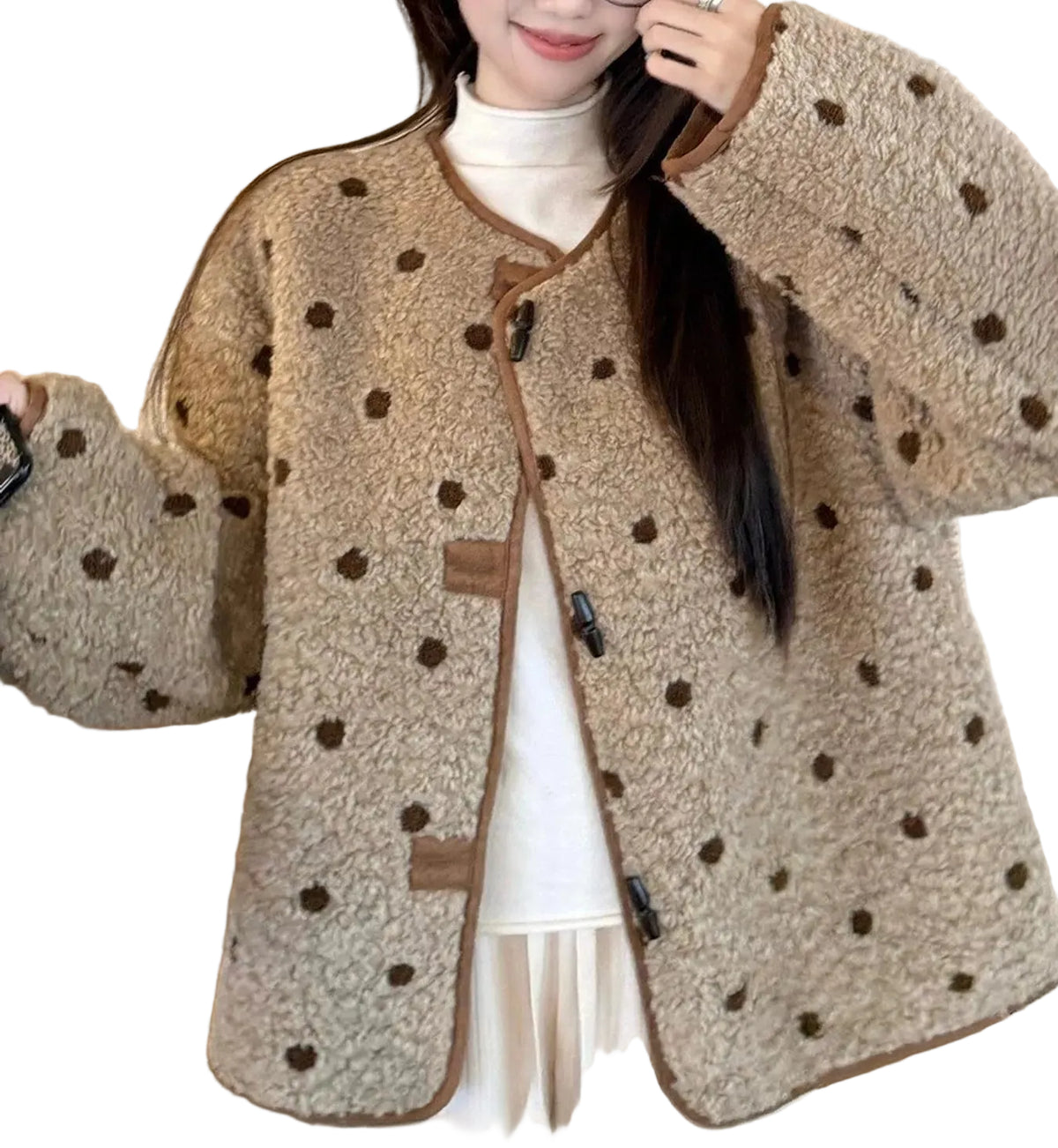 A woman wearing a beige fuzzy cropped jacket with dark brown polka dots and brown trim, layered over a white mock neck top and white pants.