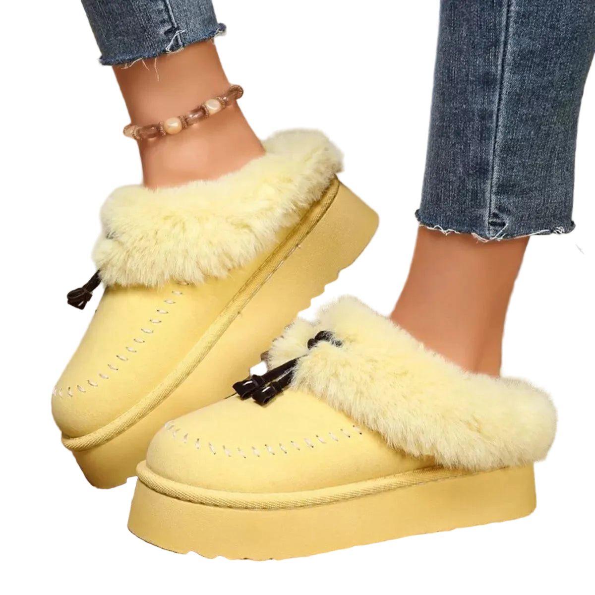A pair of yellow faux-suede platform slip-on slippers with fluffy cream faux-fur trim and black tassel pulls, shown being worn with blue jeans.