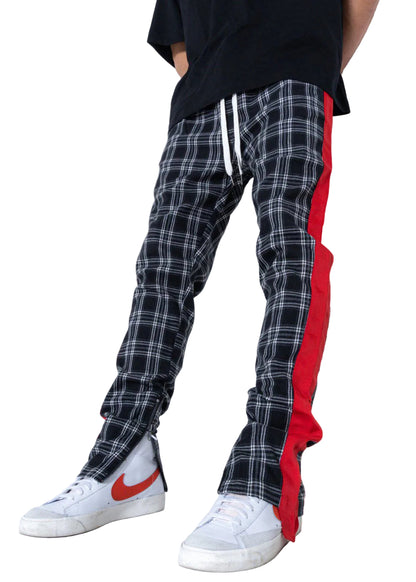 Person wearing black plaid pants with red side stripe and white sneakers on a plain background