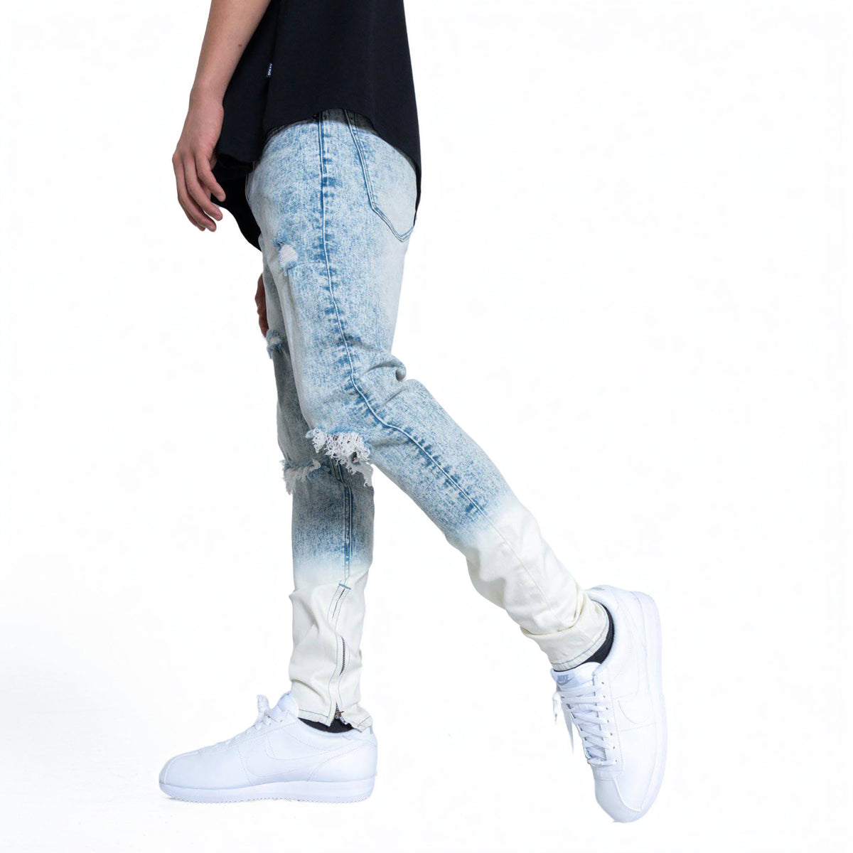 Person wearing light blue distressed jeans and white sneakers on a white background