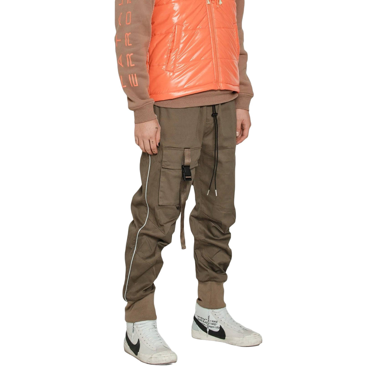 Person wearing a brown jacket with orange accents, cargo pants, and white sneakers on a white background