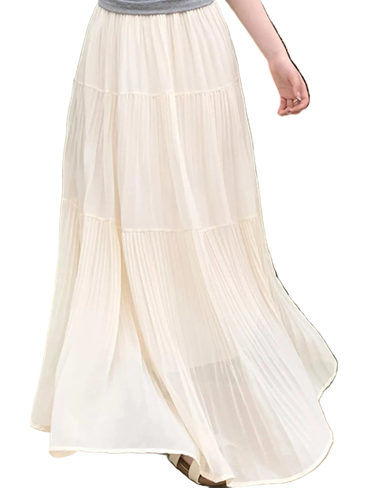 A tiered, pleated maxi skirt in a warm cream or off-white color, worn by a model standing outdoors in a garden setting.