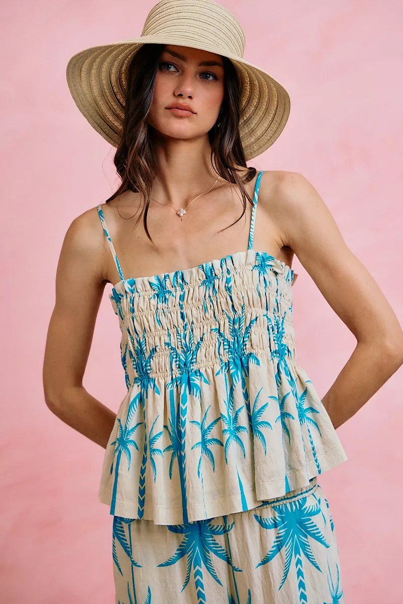 Woman wearing a palm tree patterned dress and straw hat against a pink background