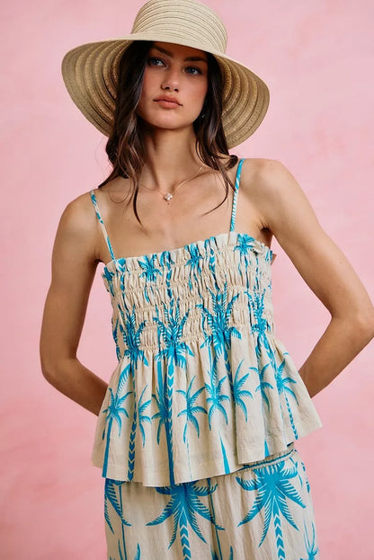 Woman wearing a palm tree patterned dress and straw hat against a pink background