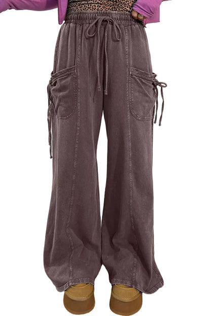 A person wearing wide-leg dusty mauve cargo pants with a drawstring waist, shown from the waist down in a styled indoor setting with a pampas grass vase and faux fur rug.