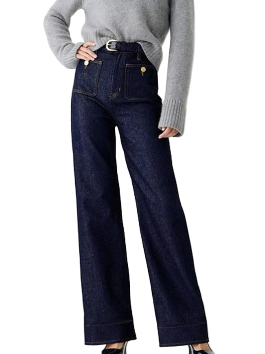 A person wearing dark indigo wide-leg jeans with a gray knit sweater, shown from the chest down against a plain light gray studio background.