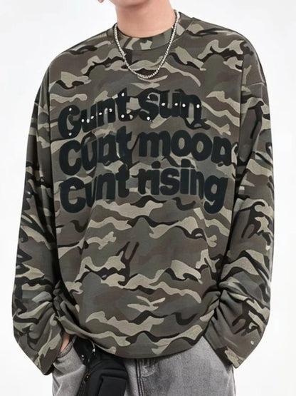 A person wearing a camouflage sweatshirt with the text 'Gunt sun Gunt moon Gunt rising' printed across the front in black. The sweatshirt features a green, brown, and gray camo pattern with black lettering.