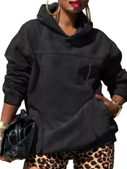 A person wearing an oversized black hooded sweatshirt with a kangaroo pocket, paired with leopard-print bottoms and holding a black textured clutch bag.